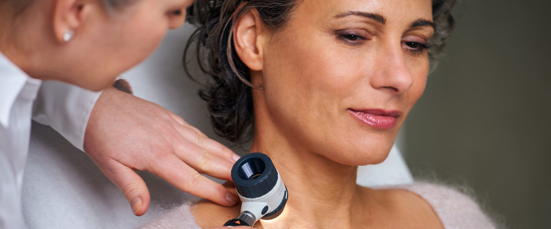 Ärztin untersucht die Haut am Hals mit dem Dermatoskop