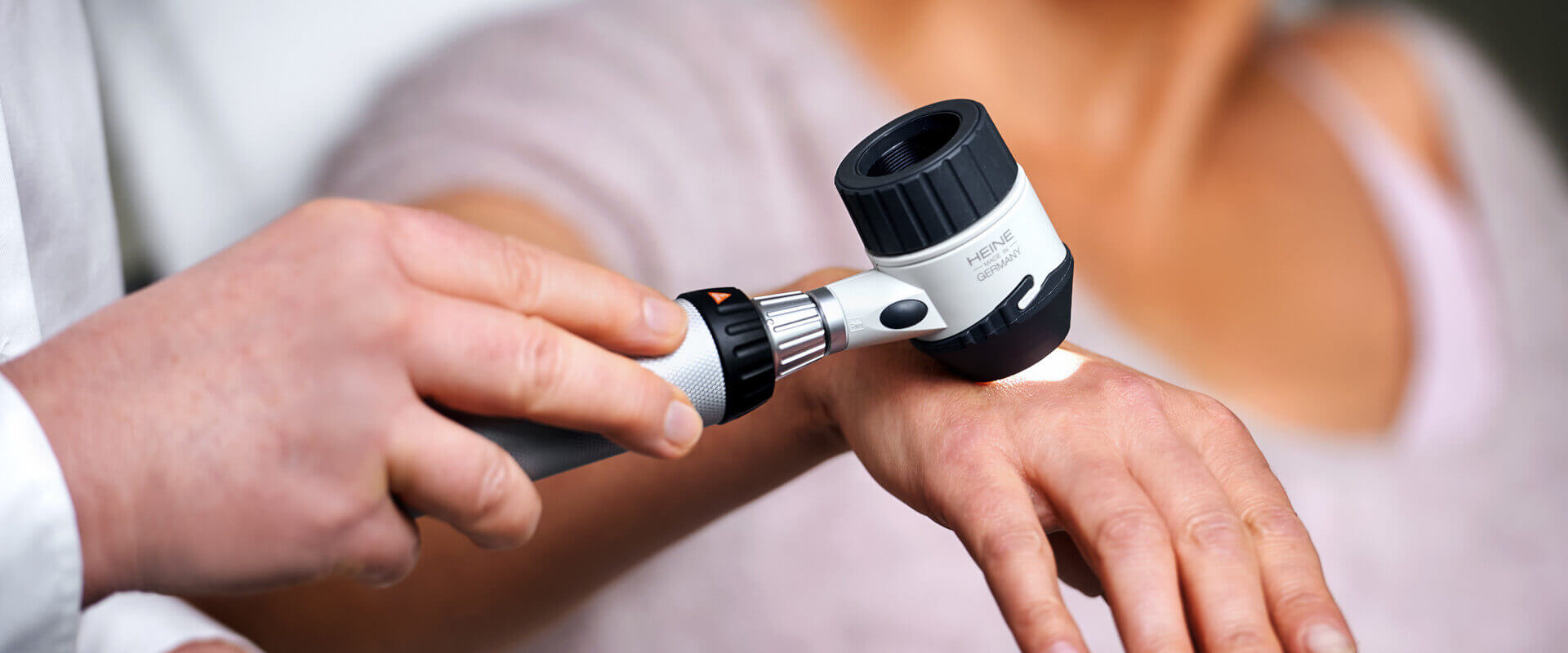 Ärztin untersucht die Haut an der Hand mit dem Dermatoskop